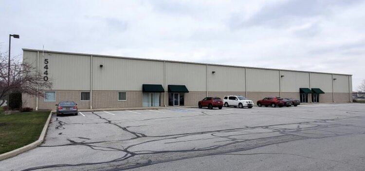 Exterior of a long single-story warehouse marked 5440, with green awnings and cars parked in front.
